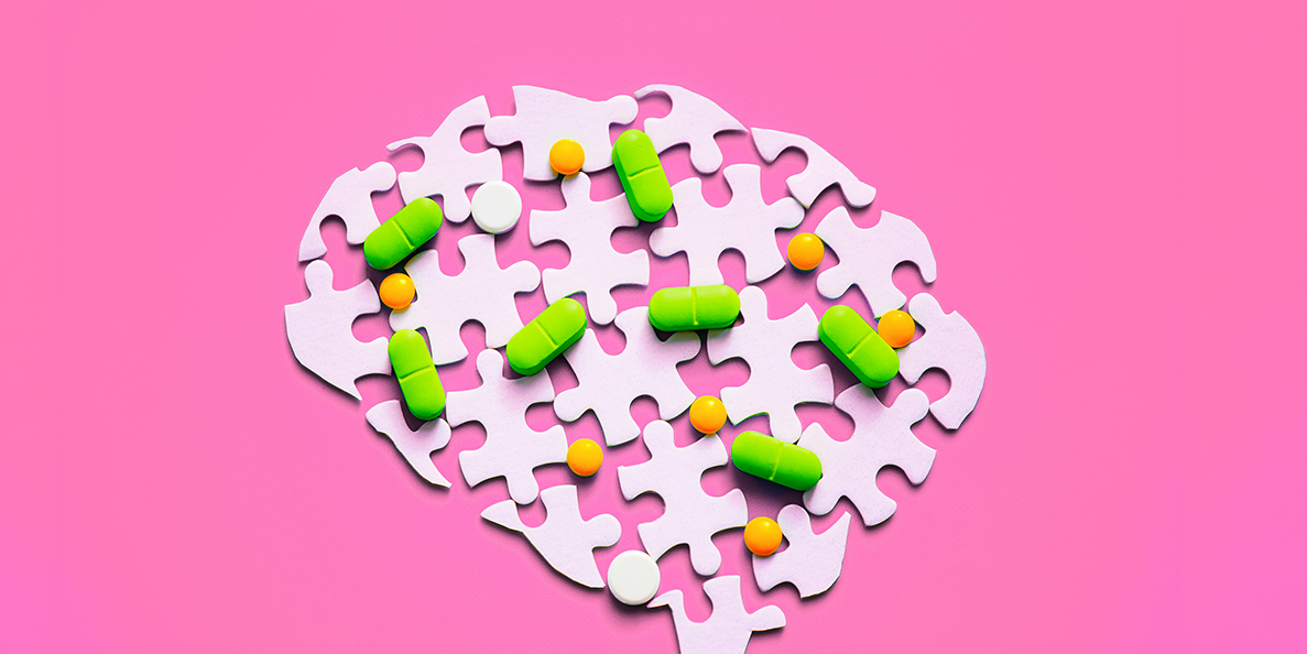 Flat-lay image of a white puzzle-piece brain silhouette with scattered green, orange, and white pills on a bright magenta background